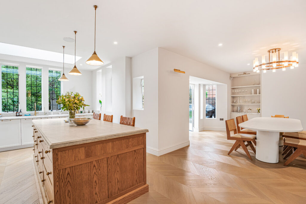 Bright modern kitchen with a large wooden island, pendant lights, a round dining table, and floor-to-ceiling windows letting in natural light.
