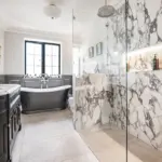 A bathroom with a dark wood vanity, a black freestanding bath, and a glass-enclosed walk-in shower with white and grey marble walls.