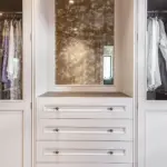 Built-in wardrobe featuring two glass-fronted clothing sections flanking a central dressing table area with four drawers and a mirror.