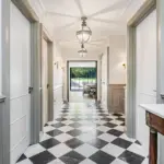A corridor with black and white chequered marble floors and panelled white doors leads to a doorway looking out onto a patio.