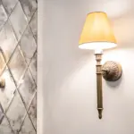 A wall-mounted light fitting with a tan fabric shade, beside a mirrored wall with a diamond pattern.