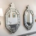 Two decorative, octagonal Venetian-style mirrors hung side by side on a wall, flanked by two matching brass wall sconces with white shades.