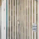 Shower enclosure with a rainfall showerhead, a handheld sprayer, and chrome controls against walls with vertical, alternating beige and white tiles.