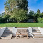 A wooden bench centred between two sets of short stone steps leading up to a green lawn.