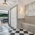 Entryway with black and white chequered marble flooring, a built-in grey bench, and a view into a dining room with a glass door.
