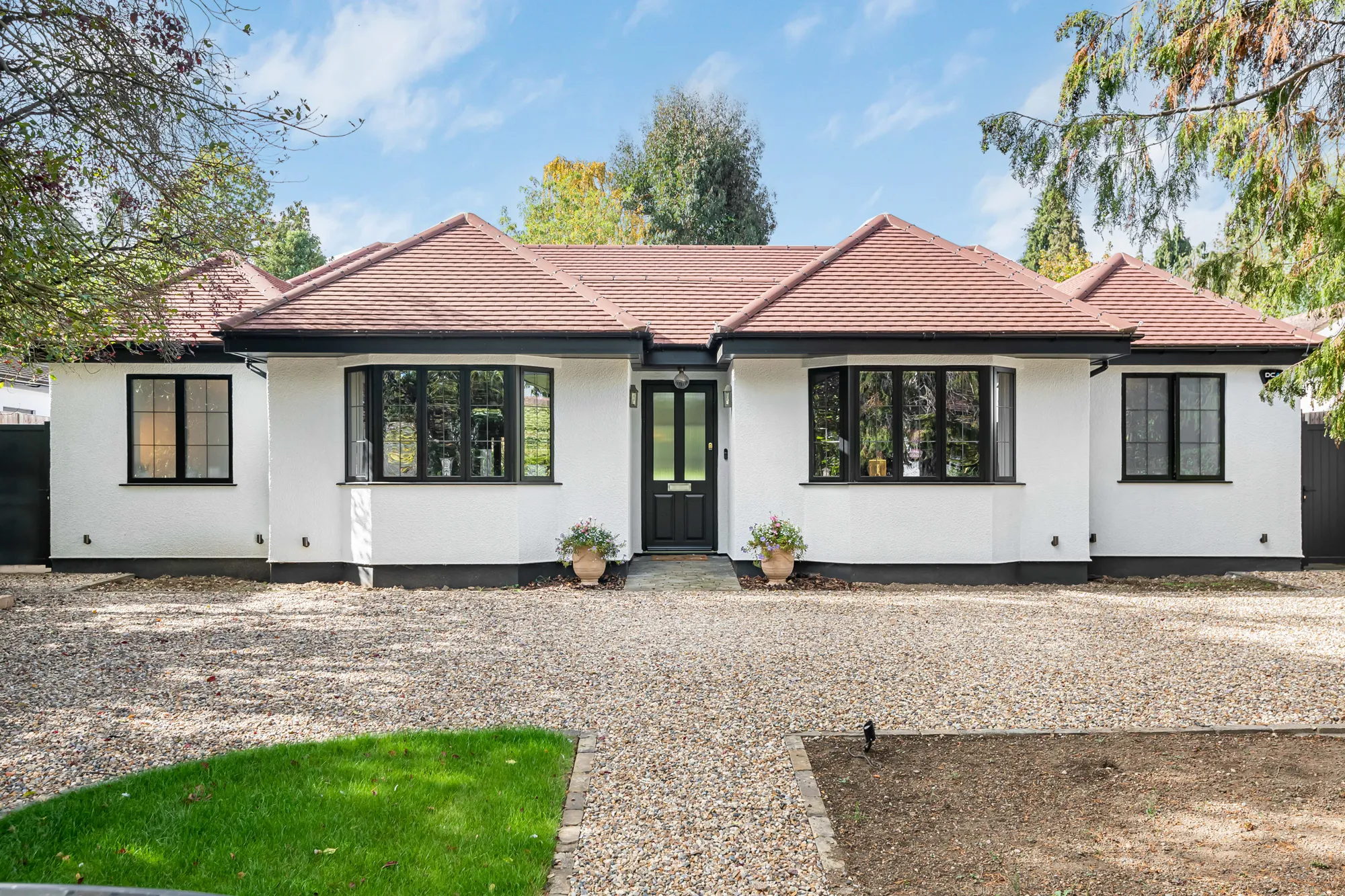 A single-storey white house with a dark tiled roof, black window frames, and a central black front door, fronted by a gravel drive.