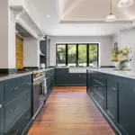 Modern kitchen with dark teal cupboards, a butler sink, a gas cooker, and a large central island with a white worktop.