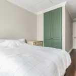 A bedroom with a bed covered in a white quilted duvet, flanked by light-coloured bedside tables, and featuring tall green double doors.