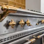 Stainless steel professional cooker with gold-toned knobs and a towel draped over the oven handle.
