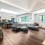 Open-plan living space with a grey corner sofa, wooden dining table, and a kitchen with blue cupboards.