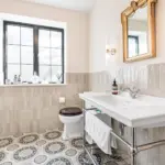A bathroom with a wall-mounted white console basin, a toilet with a dark wooden seat, and patterned floor tiles.