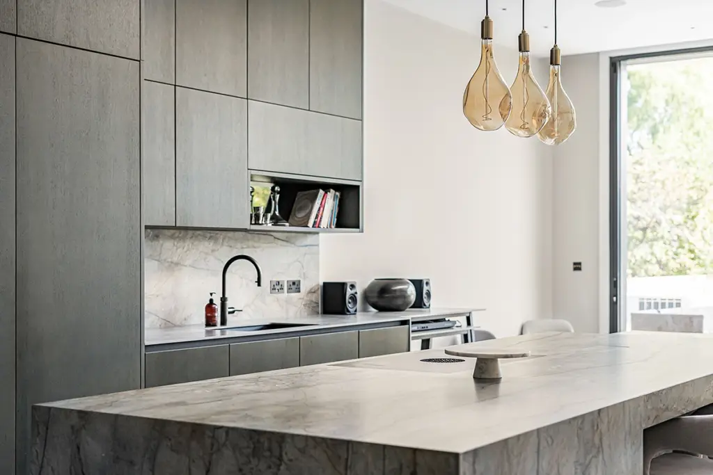 A modern kitchen with floor-to-ceiling grey cupboards, a marble-patterned island, and three glass pendant lights.