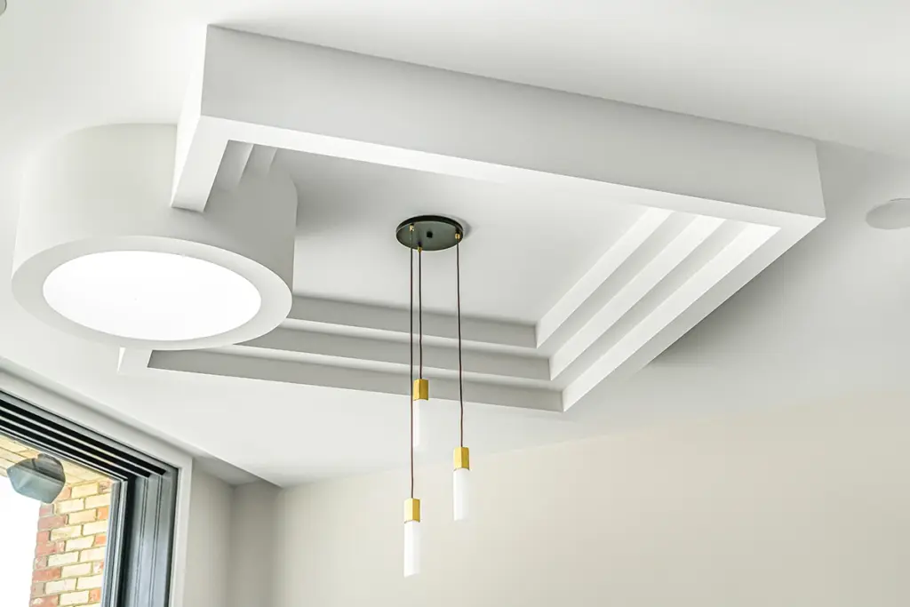 A tiered white ceiling tray featuring a round flush-mount light and a modern triple pendant light with gold accents.