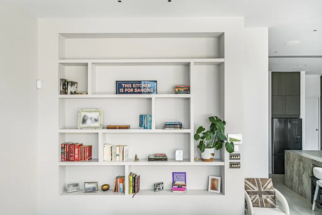 White built-in shelving unit featuring books, decorative objects, a houseplant, and a sign that reads THIS KITCHEN IS FOR DANCING.