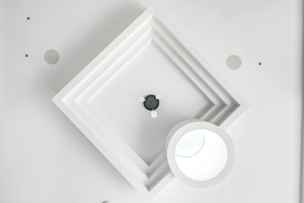 A white ceiling feature with a recessed square design, a small centre fitting, and an adjacent cylindrical light.