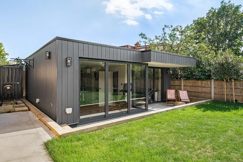 A modern charcoal-coloured garden studio with large sliding glass doors, situated in a grassy back garden.