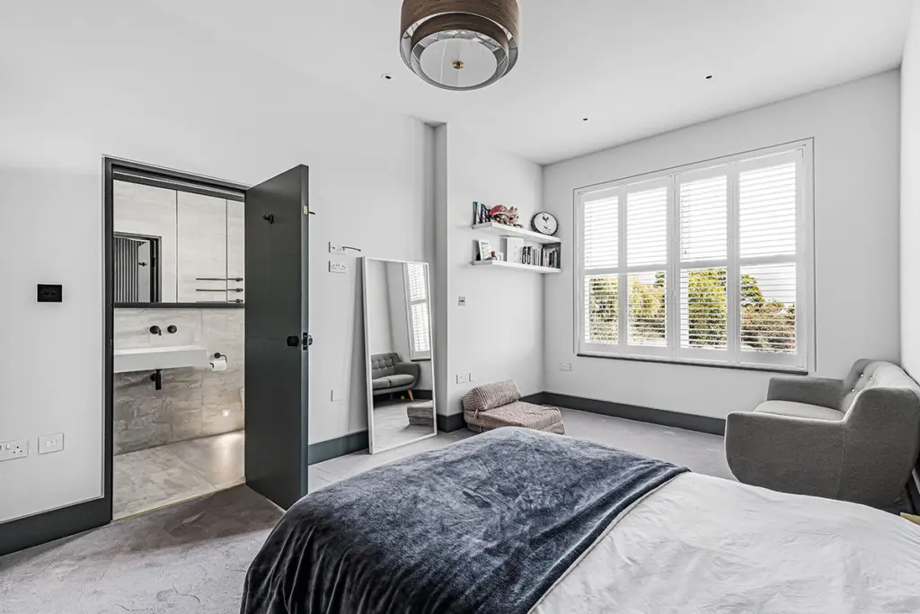 A bedroom with a bed, a small sofa, a leaning floor mirror, and an open doorway leading to a bathroom.