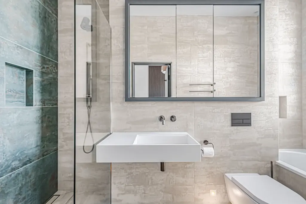 Modern bathroom featuring a wall-mounted white basin, a glass-enclosed shower with blue-green tiling, a medicine cabinet mirror, and a wall-mounted toilet.