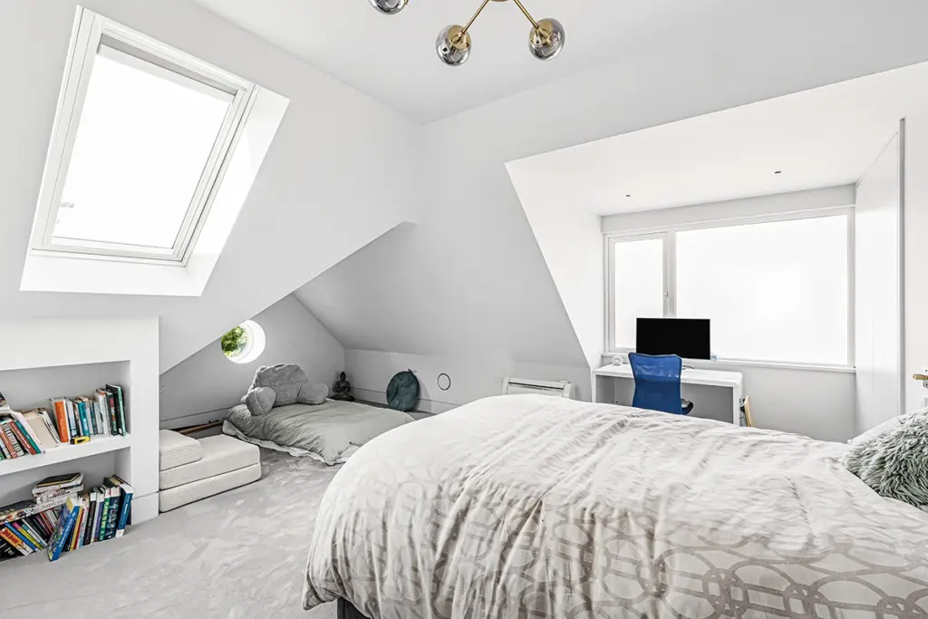 Attic bedroom featuring a bed, a small desk with a blue chair, a floor-level seating area with cushions, and built-in bookshelves.