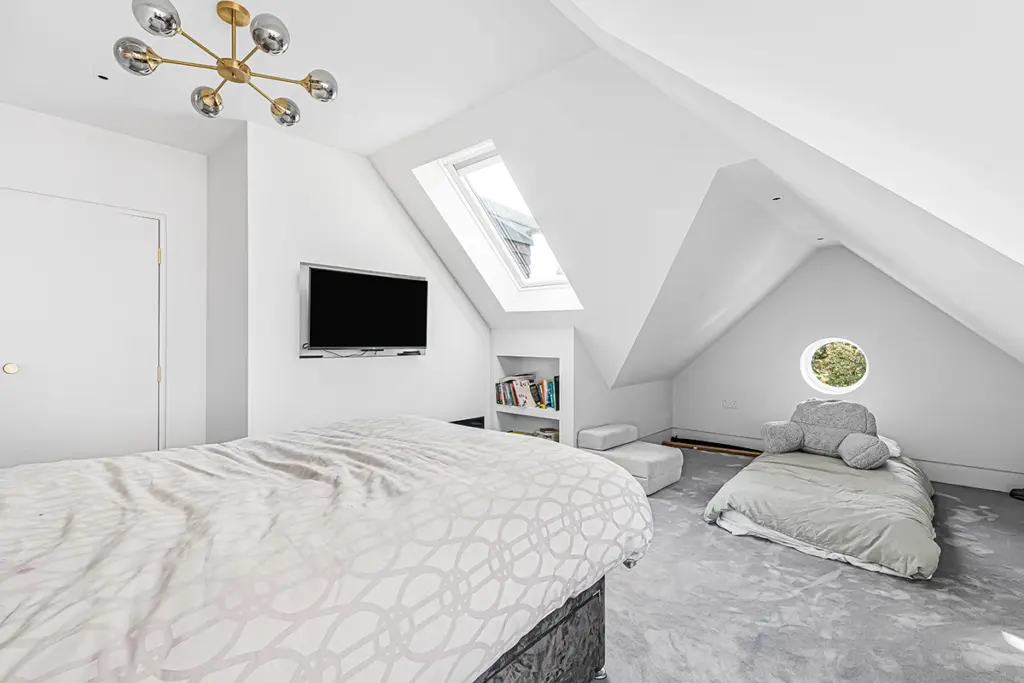 Attic bedroom with a large bed, a smaller floor mattress in the corner, a wall-mounted television, and a skylight.
