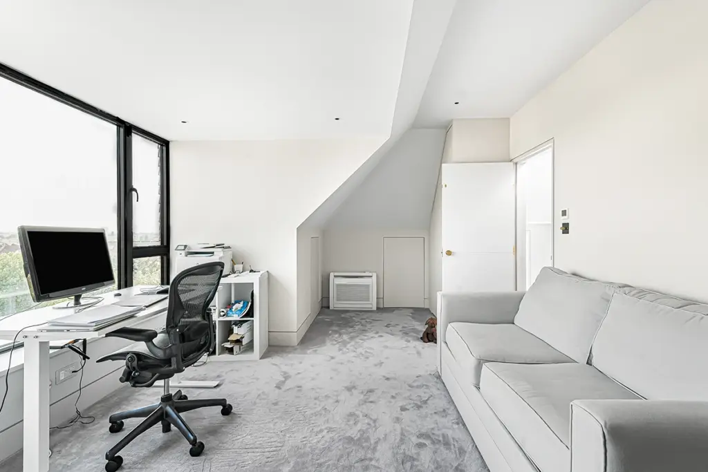 A home office space featuring a desk with a computer, an office chair, a white storage unit, and a grey sofa on a carpeted floor.