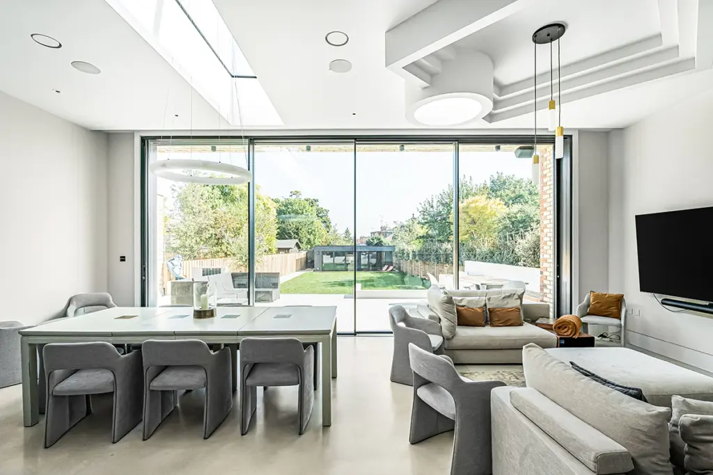 A modern open-plan living and dining area with floor-to-ceiling sliding glass doors opening to a back garden.