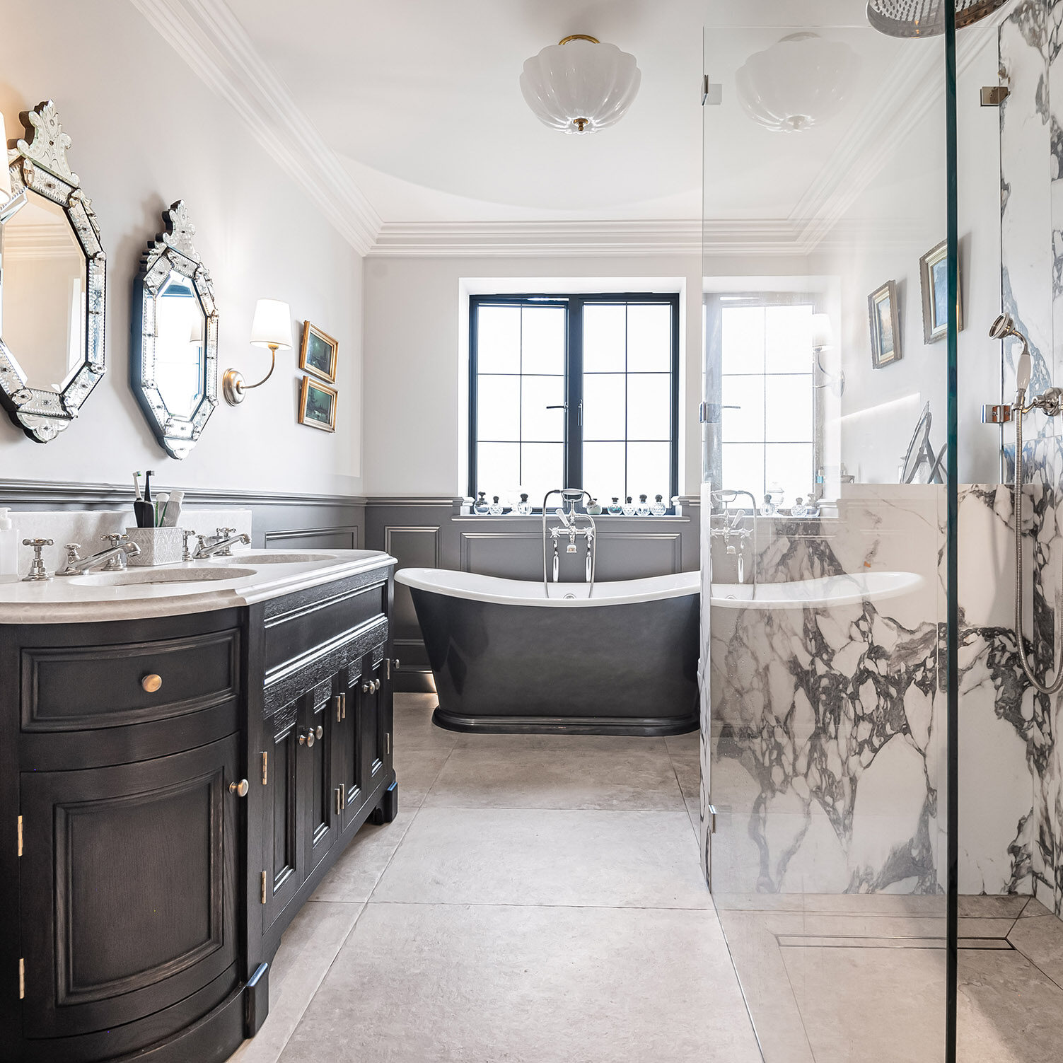 A luxury bathroom featuring a dark vanity with a marble worktop, a freestanding black bath, and a large marble-tiled walk-in shower.